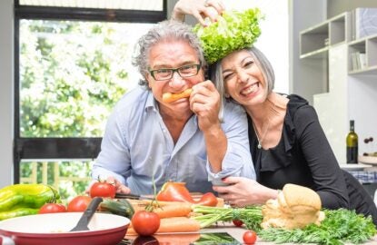 Senior couple having fun in kitchen with healthy food - Retired people cooking meal at home with man and woman preparing lunch with bio vegetables - Happy elderly concept with mature funny pensioner